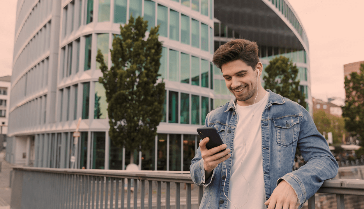 A man standing behind a street looking at his phone and smiling