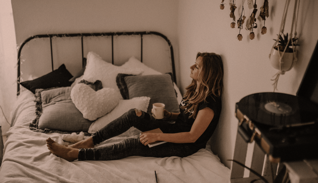A woman sitting on a bed and holding a cup in her hand thinking about something