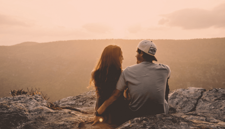 A couple sitting on the end of a mountain looking at each other